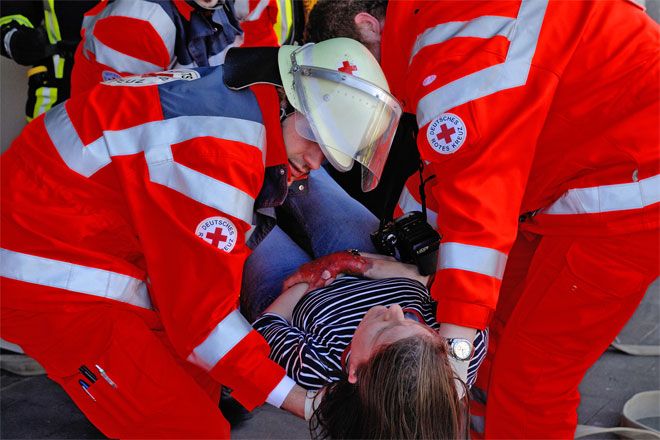 Foto: Bei einer Helferübung zum Thema Brandanschlag tragen zwei DRK-Einsatzkräfte eine Frau aus der Gefahrensituation. Sie stützen vor allem den Kopf der Frau.